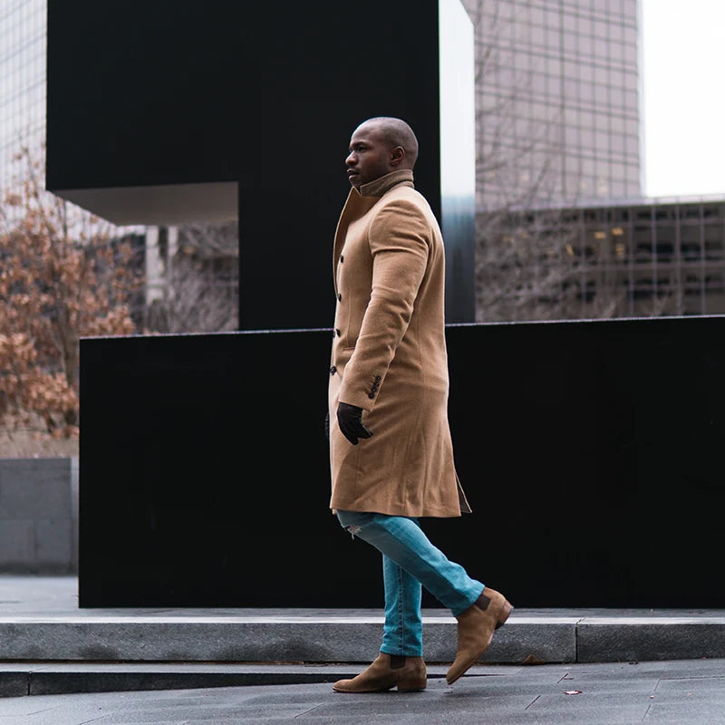 Lifestyle image of man strolling with beige overcoat, blue jeans and brown Nubuck Chelsea boots.